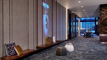 A modern hotel lobby with a patterned carpet, seating area with cushions, and a projection screen displaying a person.