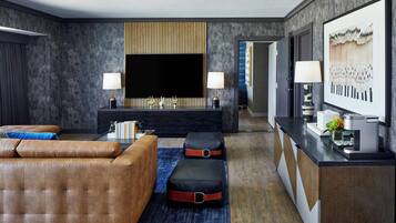 Un salon moderne doté d’un grand téléviseur à écran plat, d’un canapé, de poufs, d’une table basse et d’un buffet surmonté d’une lampe.