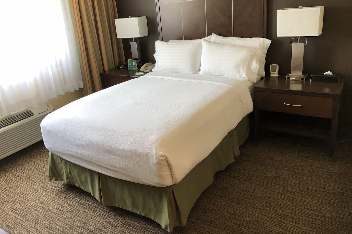 A hotel room with a large bed, two bedside tables, a nightstand, a lamp, and a telephone.
