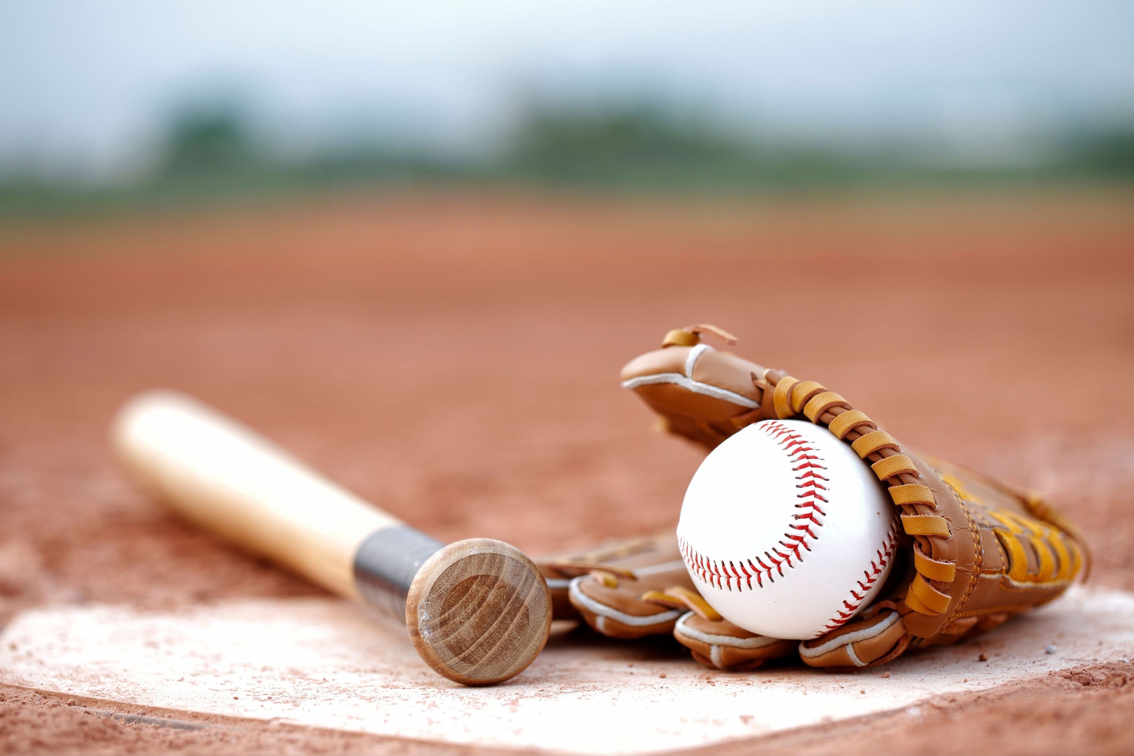 A baseball bat, a glove, and a ball on a dirt field.