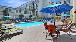 Un espace piscine d’hôtel avec des chaises longues et des parasols, entouré d’un bâtiment doté de nombreuses fenêtres et de balcons.