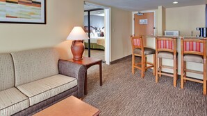 A hotel room with a sofa, a small table with a lamp, a kitchenette with a microwave, and a bed visible through an open door. - Holiday Inn Hotel & Suites Anaheim by IHG (Anaheim)