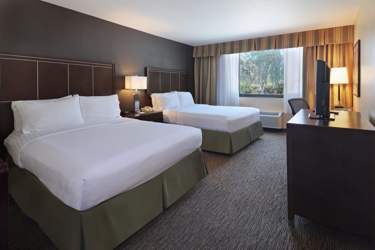 A hotel room with two beds, a desk, a chair, a TV, and a window with curtains.