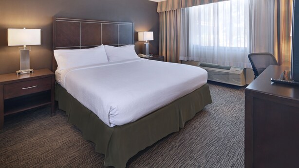 A hotel room with a large bed, two bedside tables with lamps, a desk, and a window with curtains. - Holiday Inn Hotel & Suites Anaheim by IHG (Anaheim)
