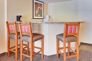 A corner seating area with two wooden chairs with striped cushions, a small bar counter, a coffee machine, and a microwave. - Holiday Inn Hotel & Suites Anaheim by IHG (Anaheim)
