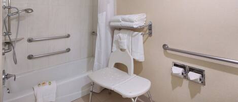 A bathroom with a shower, grab bars, a wheelchair-accessible bench, and a toilet with a paper towel dispenser.
