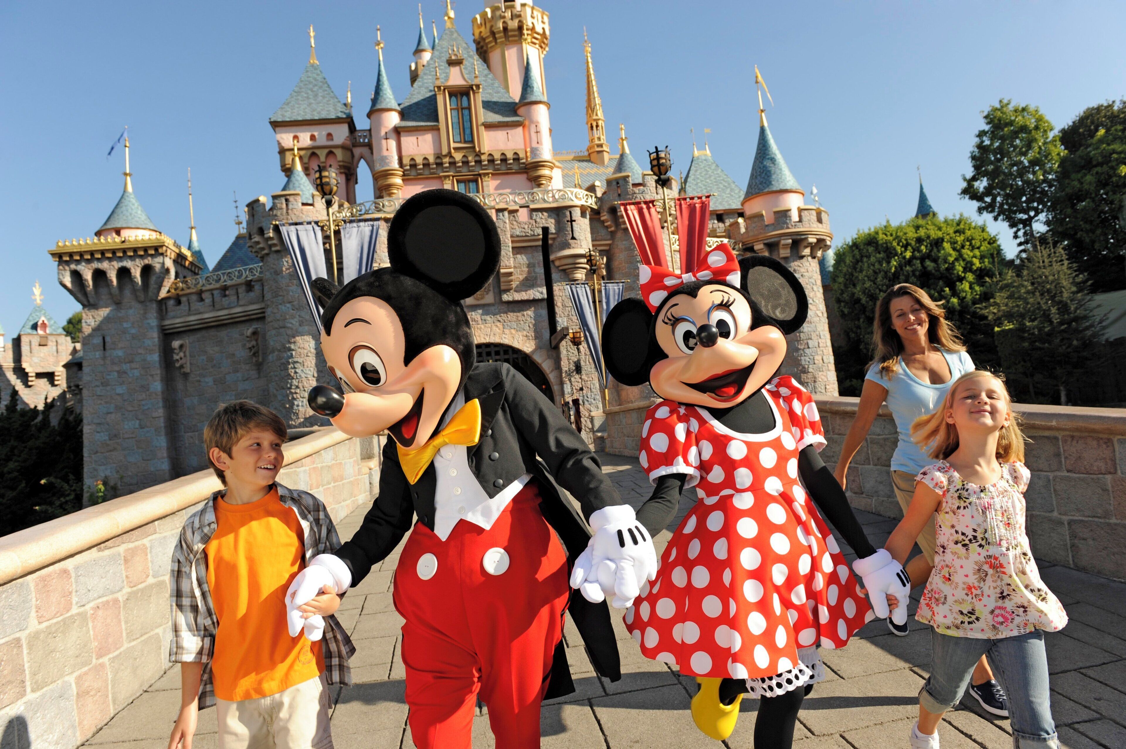 Mickey and Minnie Mouse characters with children in front of a castle-like building.