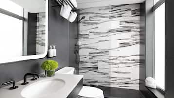 A modern bathroom with a large mirror, a white sink, a toilet, and a shower area with a marble wall.