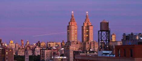 Un horizonte urbano al atardecer con edificios destacados, incluyendo dos torres altas con agujas, y un tanque elevado de agua.