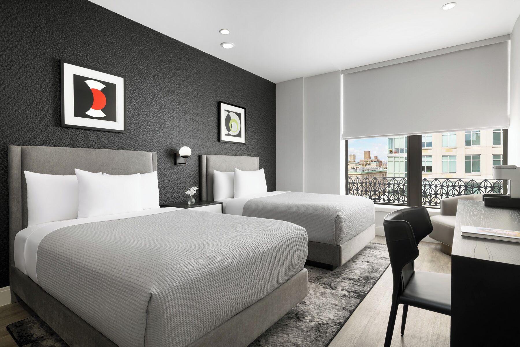 Une chambre d’hôtel moderne avec deux lits, un bureau et un balcon offrant une vue sur la ville.