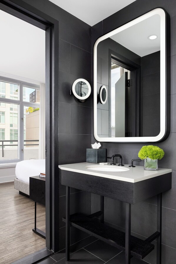 A modern bathroom with a large mirror, black tiles, a white sink, and a small green plant.