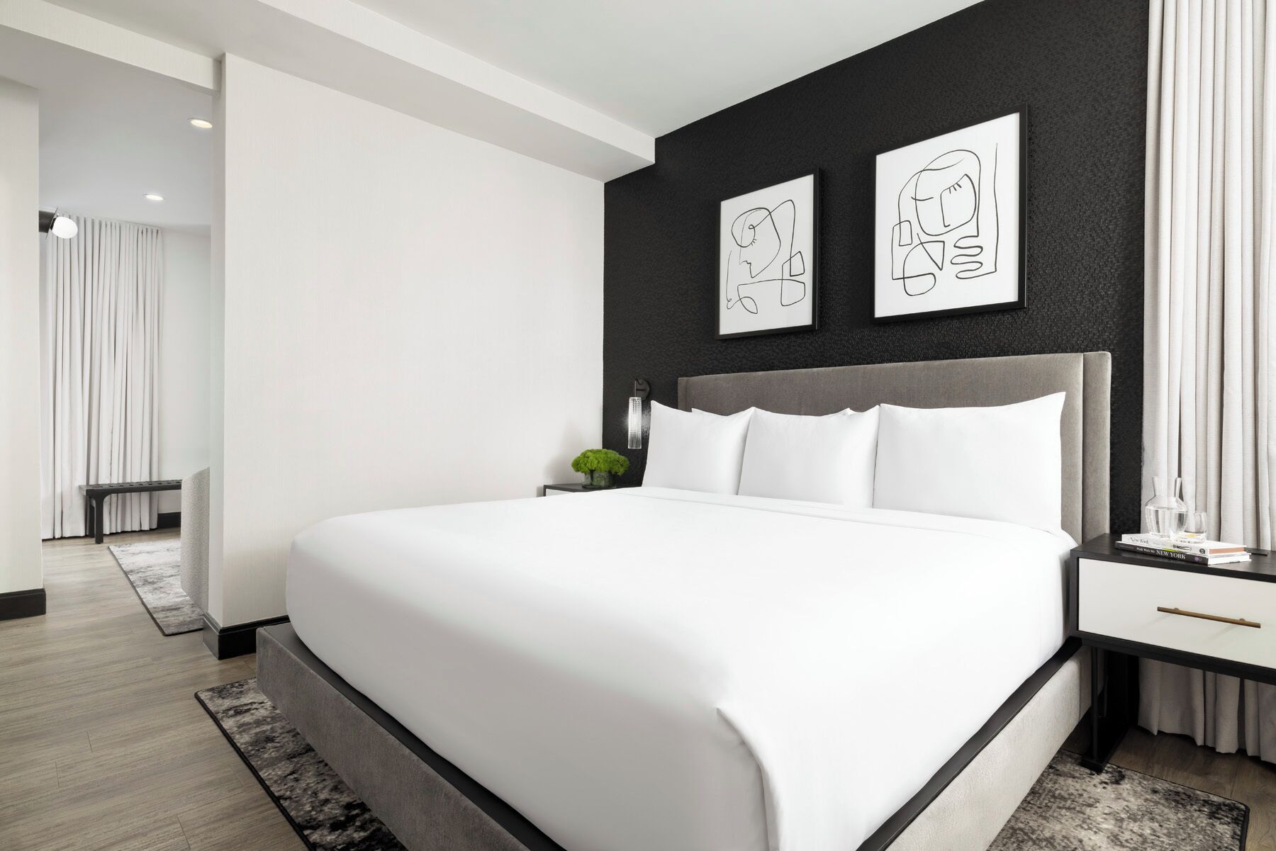 Ein modernes Schlafzimmer mit einem großen Bett, einem Nachttisch und zwei abstrakten Kunstwerken an der Wand.
