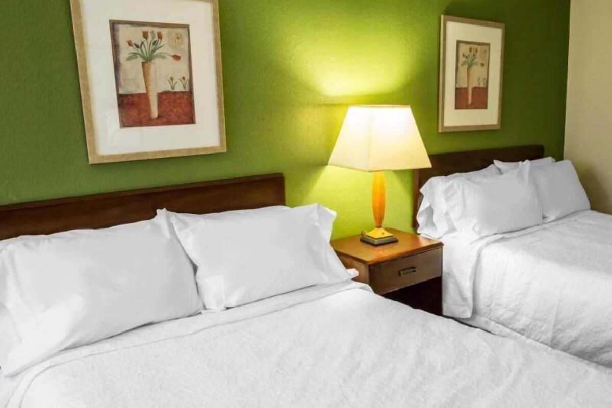 A hotel room with two beds, a nightstand with a lamp, and two framed pictures on the wall.