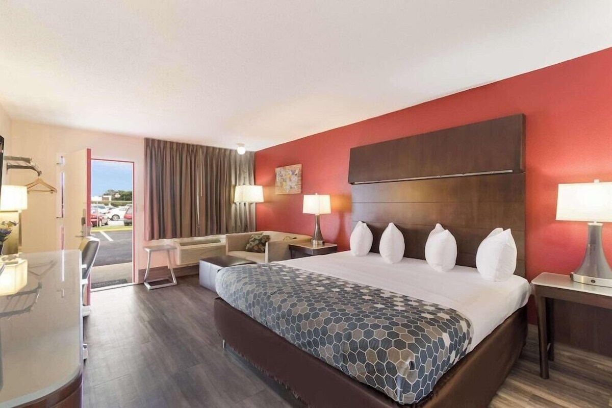 A hotel room with a bed, bedside tables, a desk, a chair, a sofa, and a view of the outside.
