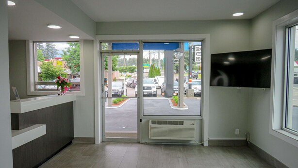 A reception area with a glass door, a reception desk, a mounted TV, and a view of the parking lot outside. - Motel 6 Tigard, OR - Portland Southwest (Tigard)