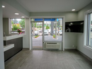 A reception area with a glass door, a reception desk, a mounted TV, and a view of the parking lot outside.