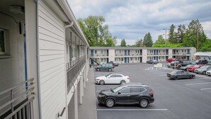 A motel with a parking lot, multiple buildings, and trees in the background. - Motel 6 Tigard, OR - Portland Southwest (Tigard)