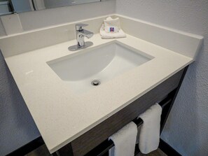 A bathroom sink with a mirror above it, a towel rack below, and a small towel dispenser.