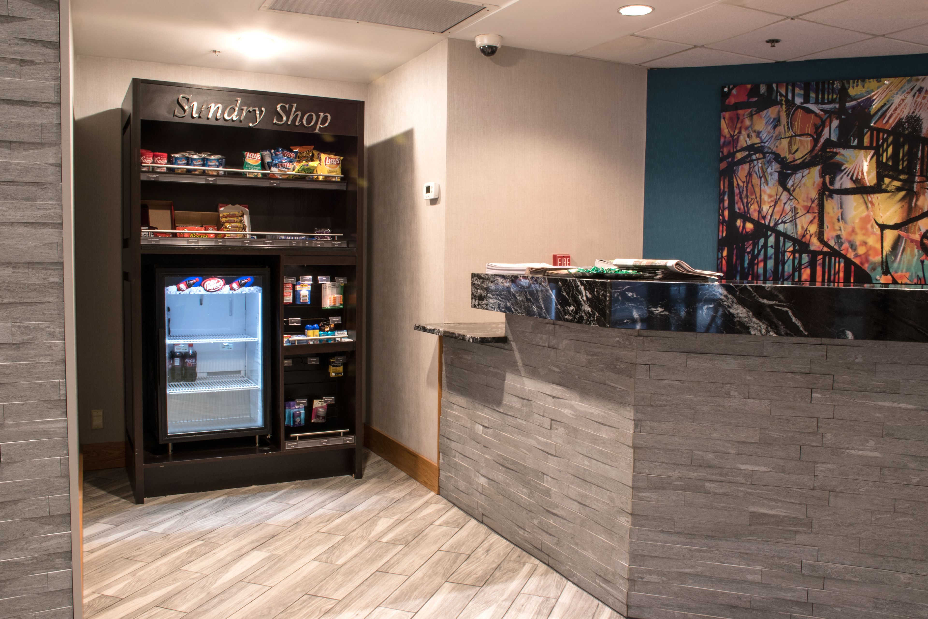 A self-service sundry shop with a variety of snacks and beverages, a marble counter, and a colorful abstract mural on the wall.