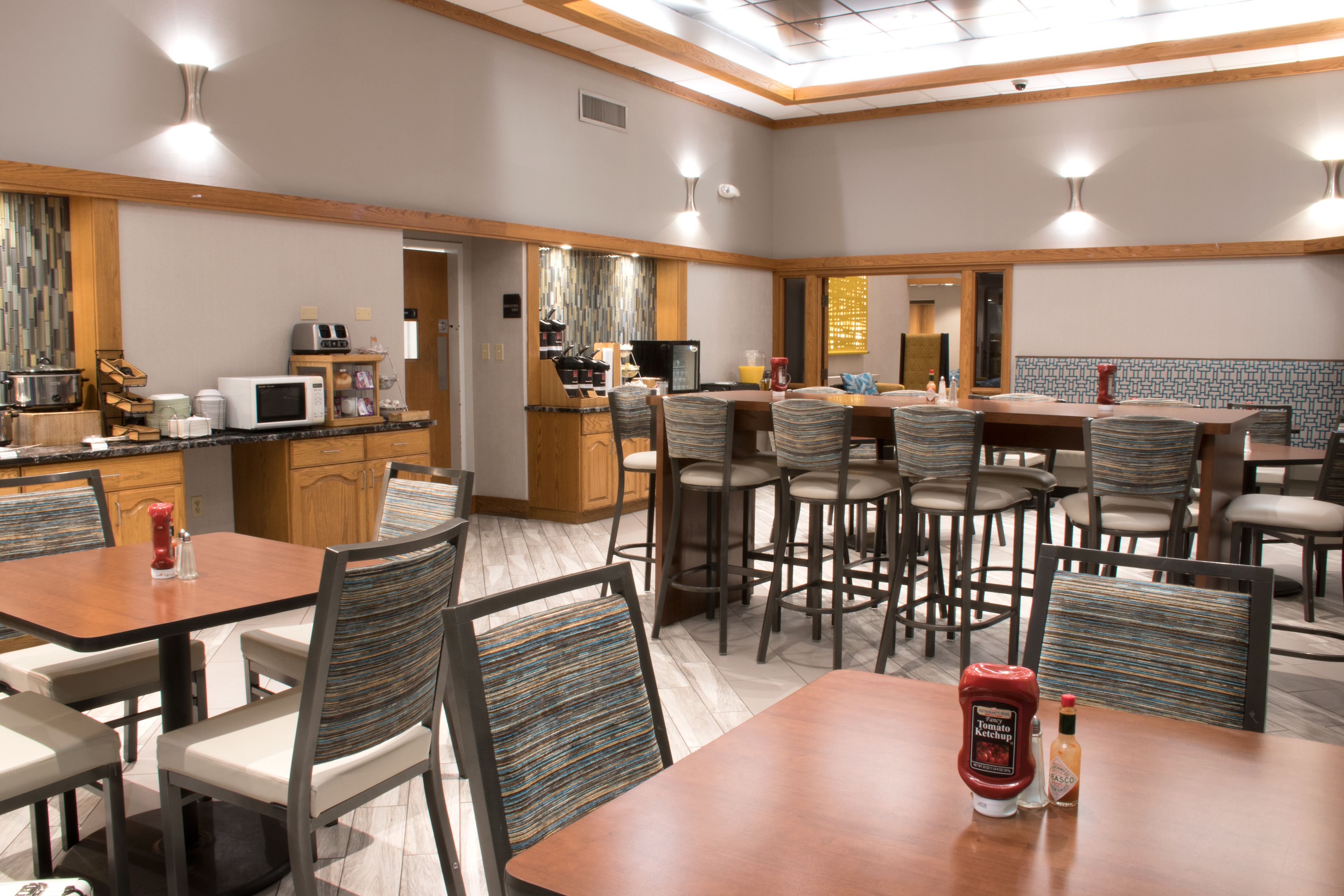 A hotel dining area with multiple tables and chairs, a kitchen area with appliances, and a bar.