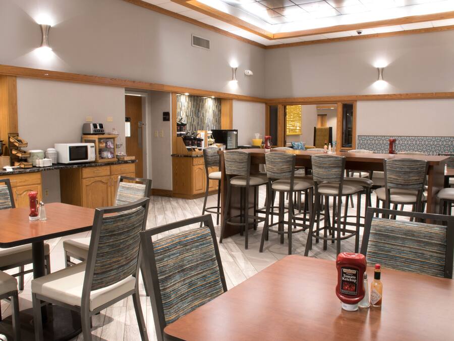 A hotel dining area with multiple tables and chairs, a kitchen area with appliances, and a bar.
