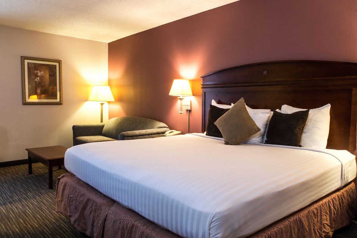 A hotel room with a large bed, two bedside lamps, a small table, and a framed picture on the wall.