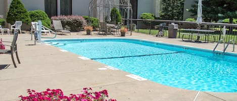 Una piscina con sillas de descanso y un pabellón, rodeada de plantas en macetas y un edificio al fondo.