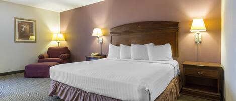 A hotel room with a large bed, two bedside lamps, a nightstand, a chair, and a telephone.