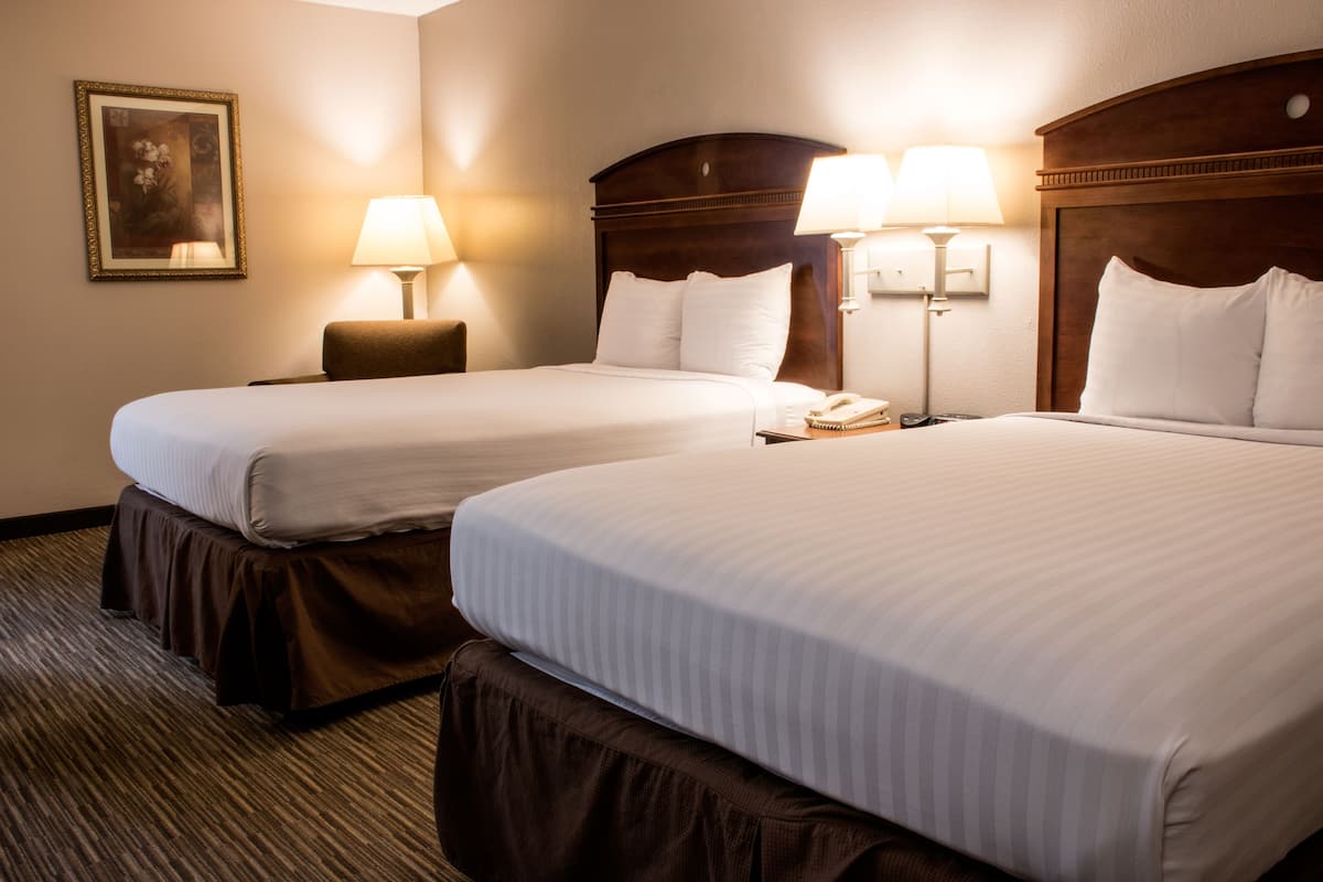 A hotel room with two beds, each with a headboard, bedside lamps, and a framed picture on the wall.