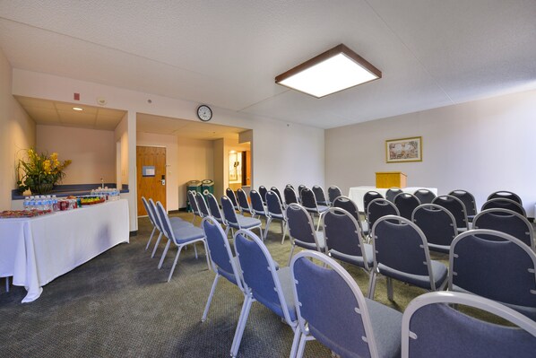 A conference room with rows of chairs, a table with water bottles, and a clock on the wall.