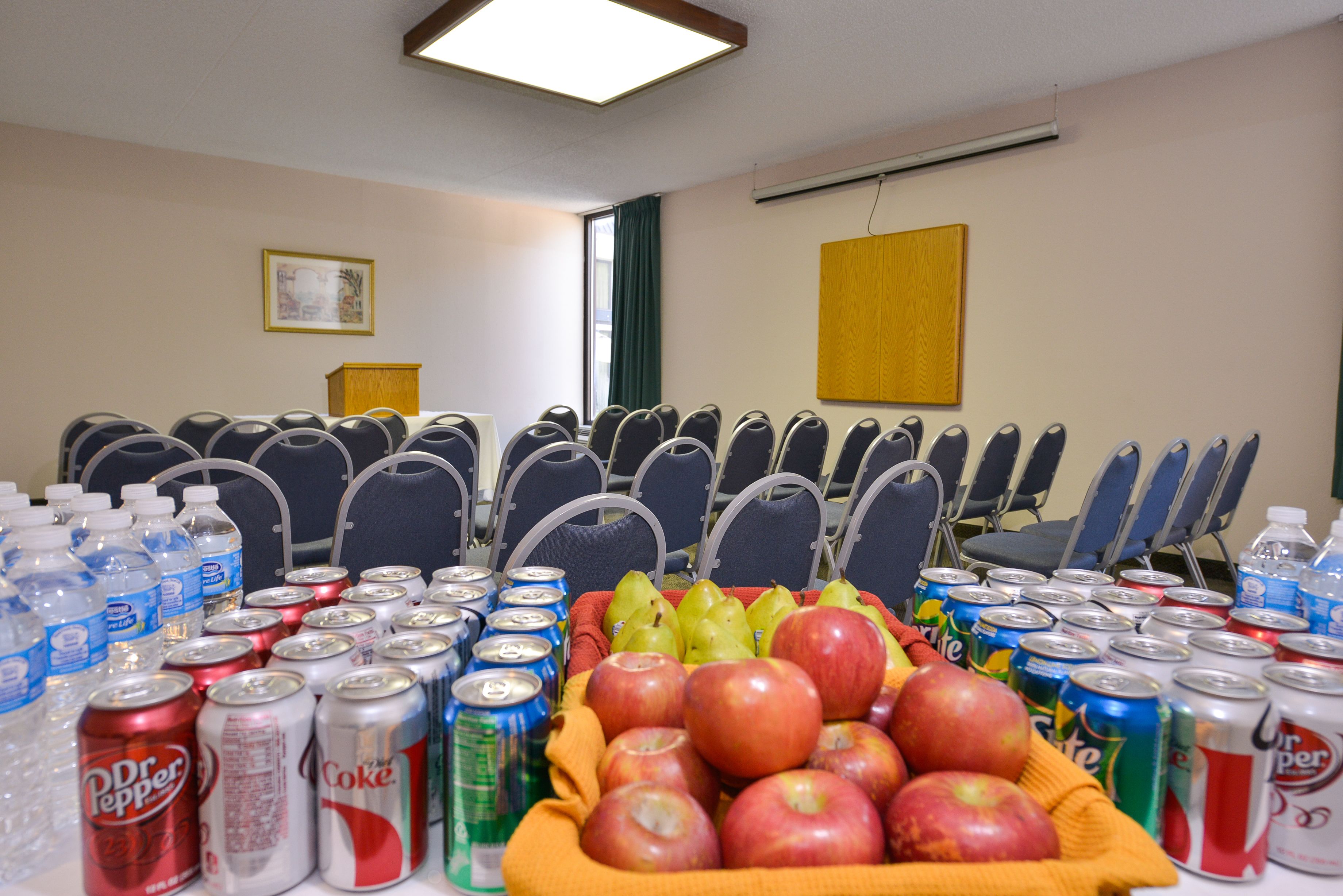 A conference room with rows of chairs, a table with beverages and fruits, and a framed picture on the wall.