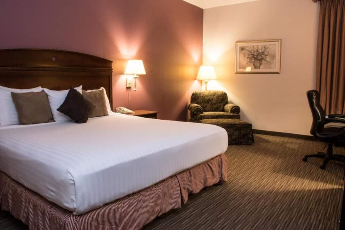A hotel room with a large bed, two bedside lamps, a chair, a small table, and a framed picture on the wall.