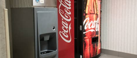 Una máquina expendedora con el logotipo de Coca-Cola, un equipo de aire acondicionado pequeño y un suelo de baldosas.