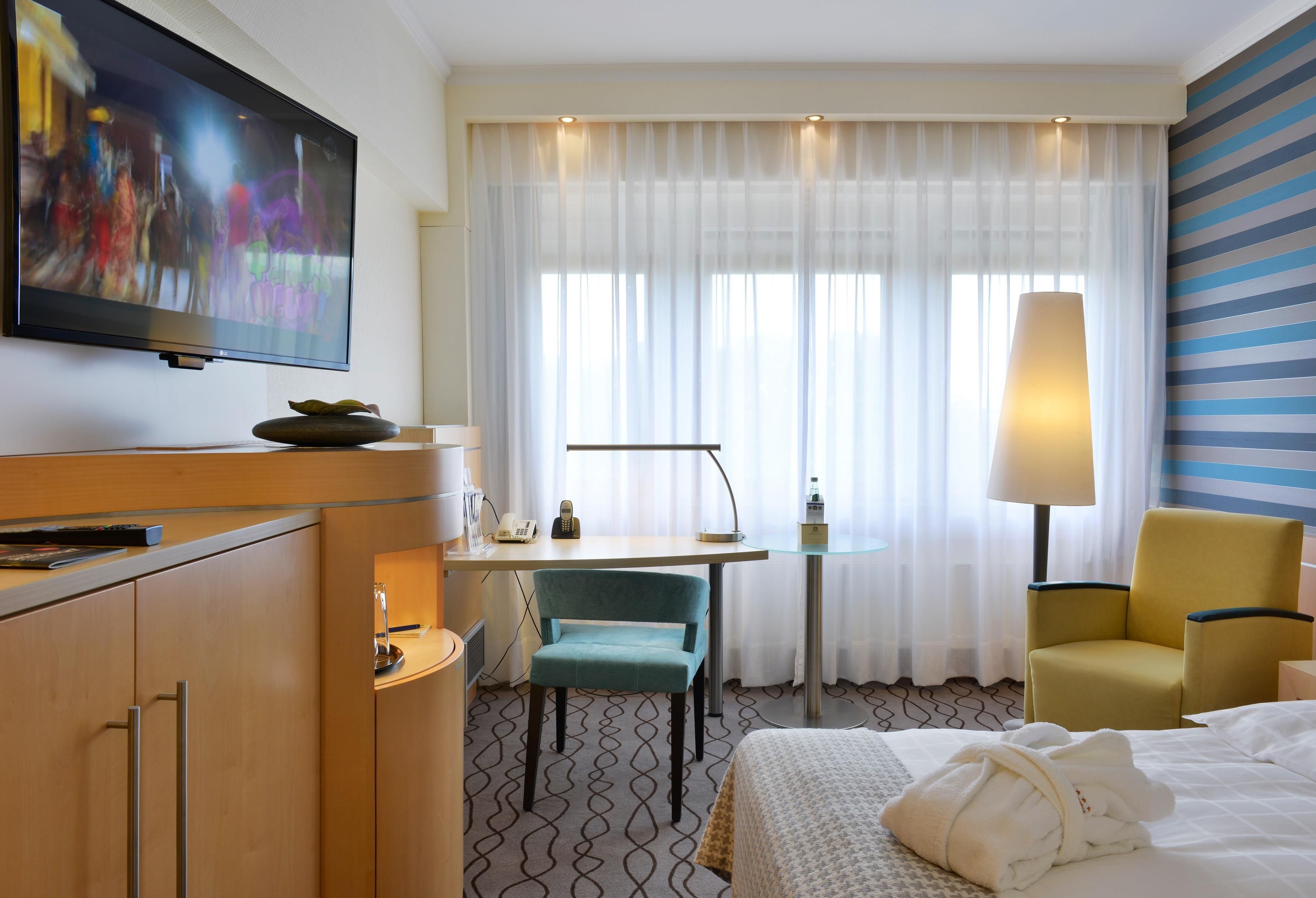 Habitación de hotel con cama, escritorio con teléfono, silla, televisor y lámpara.