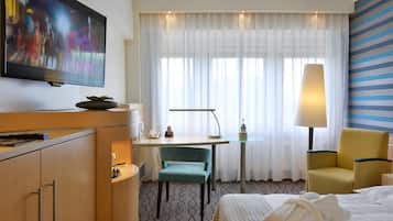 Habitación de hotel con cama, escritorio con teléfono, silla, televisor y lámpara.