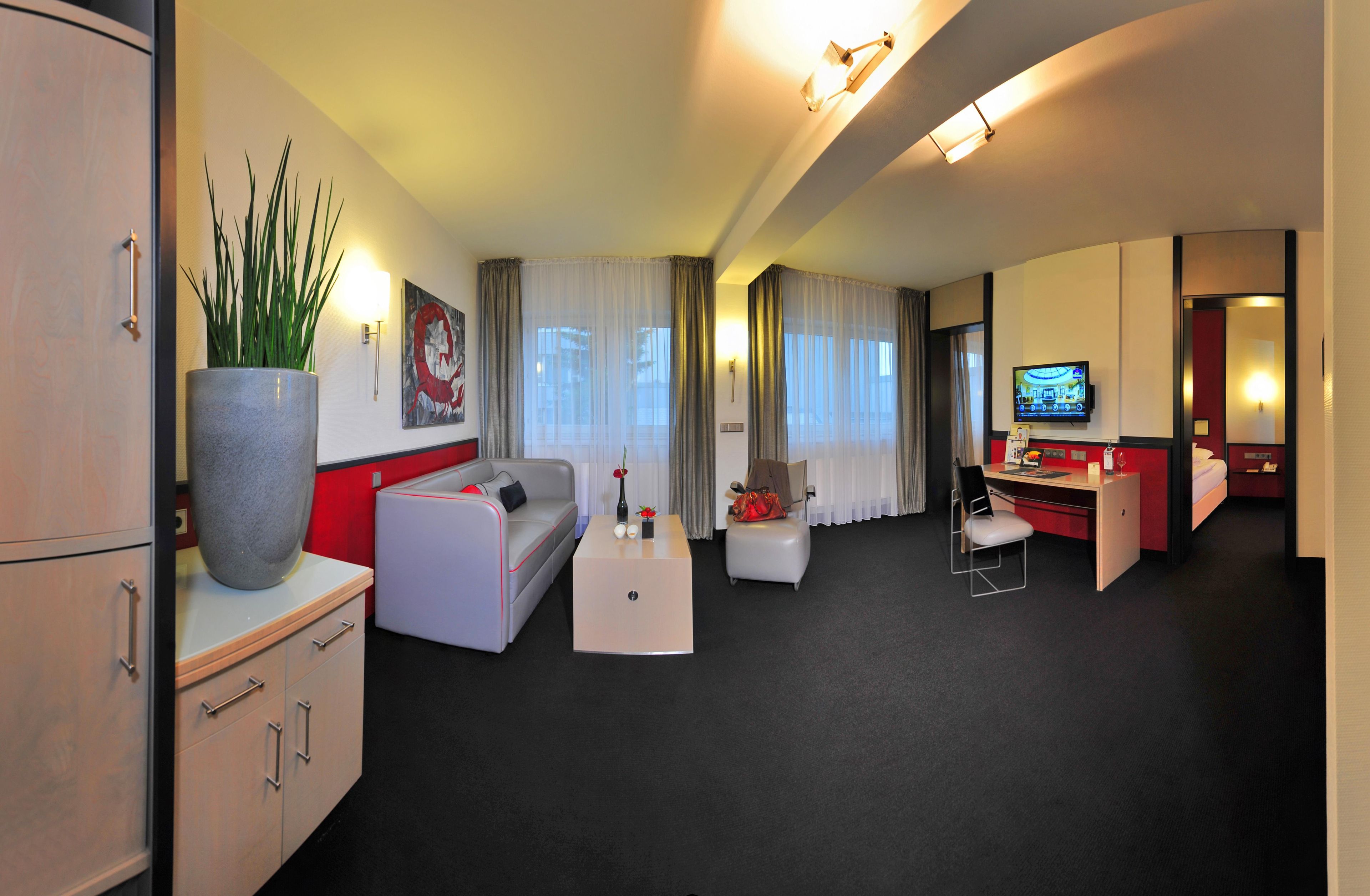 Ein Hotelzimmer mit einer Couch, einem Schreibtisch, einem Fernseher und einer großen Topfpflanze.