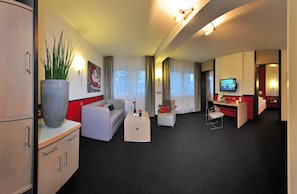Een hotelkamer met een bank, een bureau, een televisie en een grote potplant.