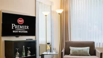 Habitación de hotel con una televisión mostrando la marca 'Premier Best Western', un sofá marrón con un cojín, una alfombra estampada y una lámpara de pie.