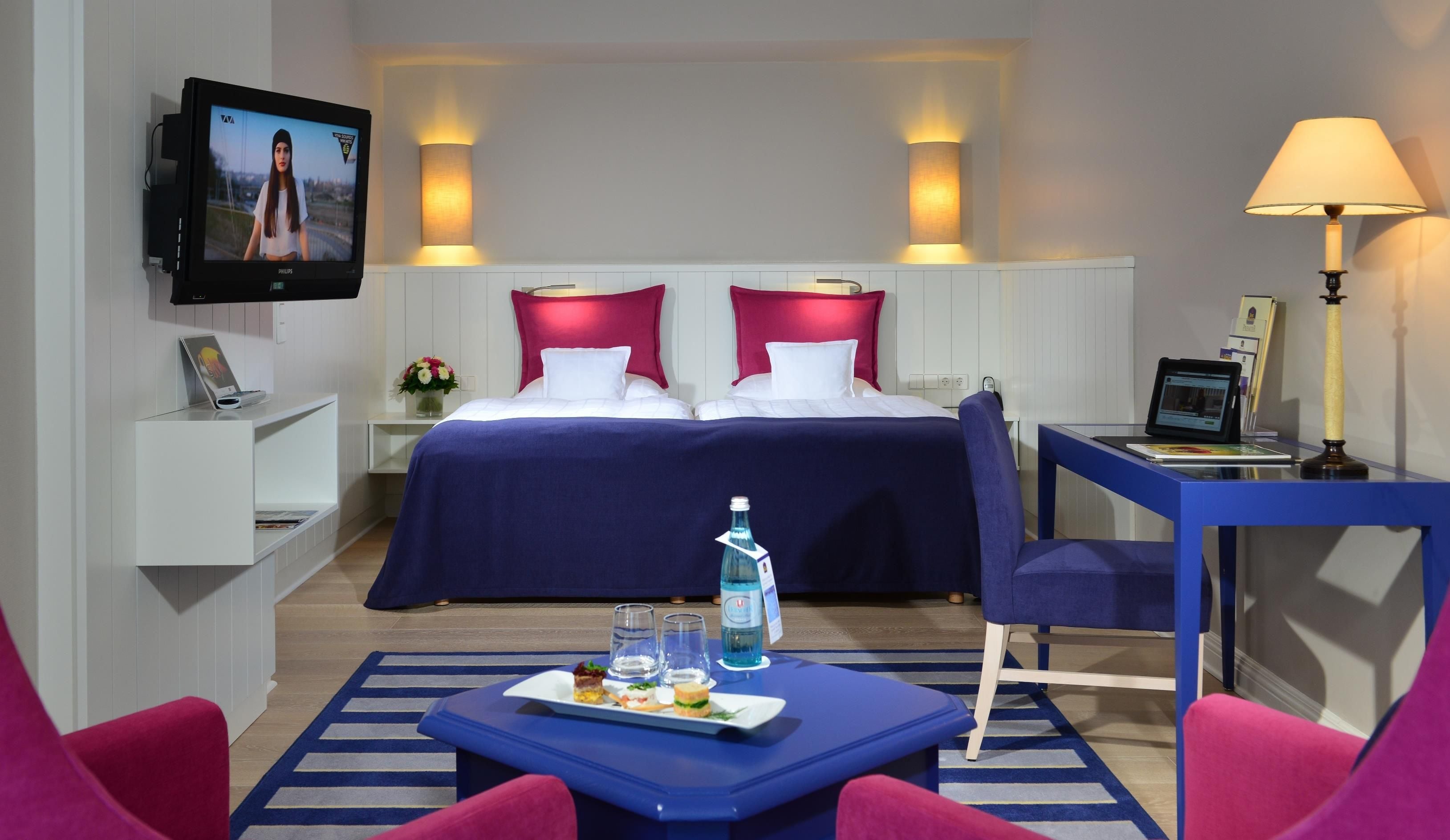 Ein Hotelzimmer mit Bett, Schreibtisch, Fernseher und einem Tisch mit Speisen und Getränken.