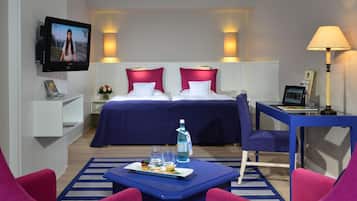 A hotel room with a bed, a desk, a TV, and a table with food and drinks.