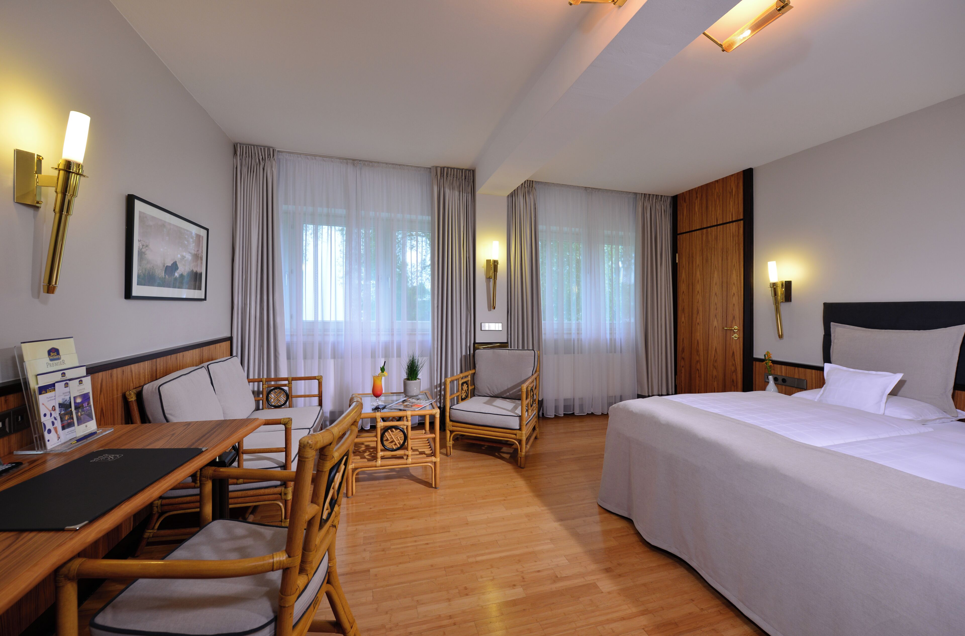 A hotel room with a bed, a desk with a chair, a small table with a chair, and a window with curtains.
