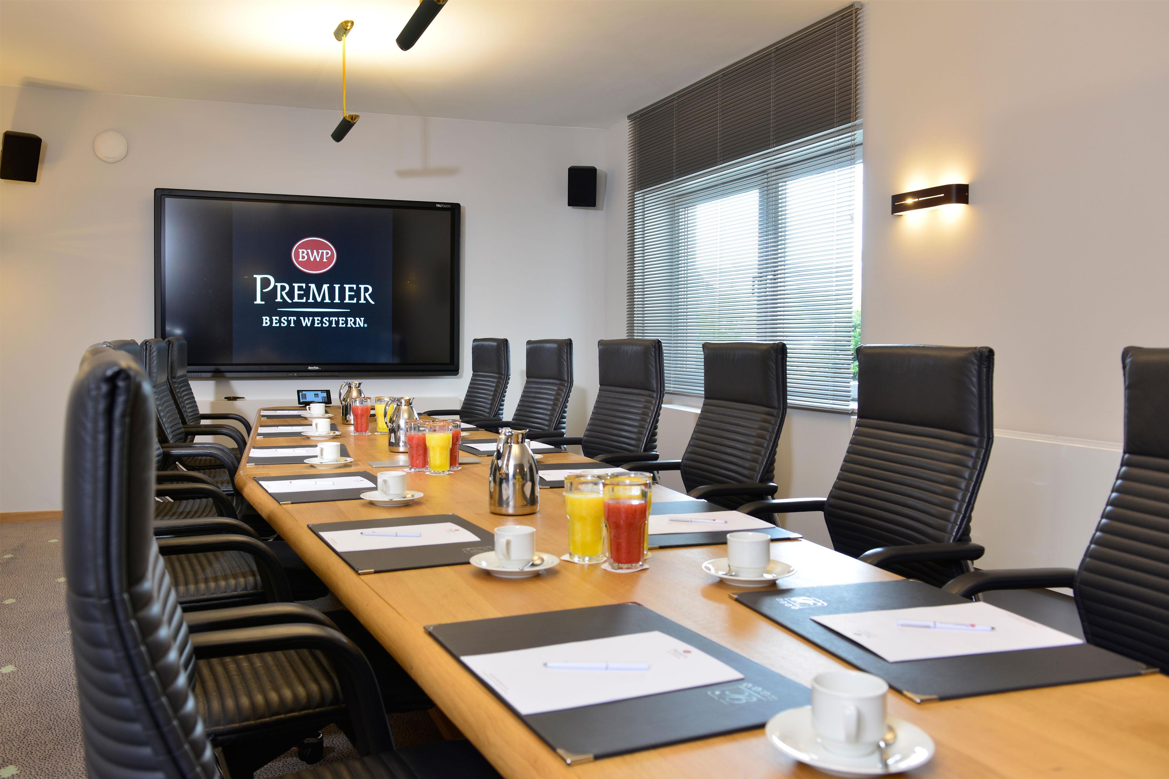 A conference room with a long table, black chairs, a large screen, and breakfast items.