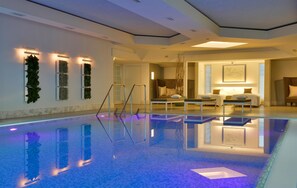 A modern indoor swimming pool with clear water, a lounge area with seating, and a staircase leading to an upper level. - Best Western Premier Parkhotel Kronsberg (Hannover)
