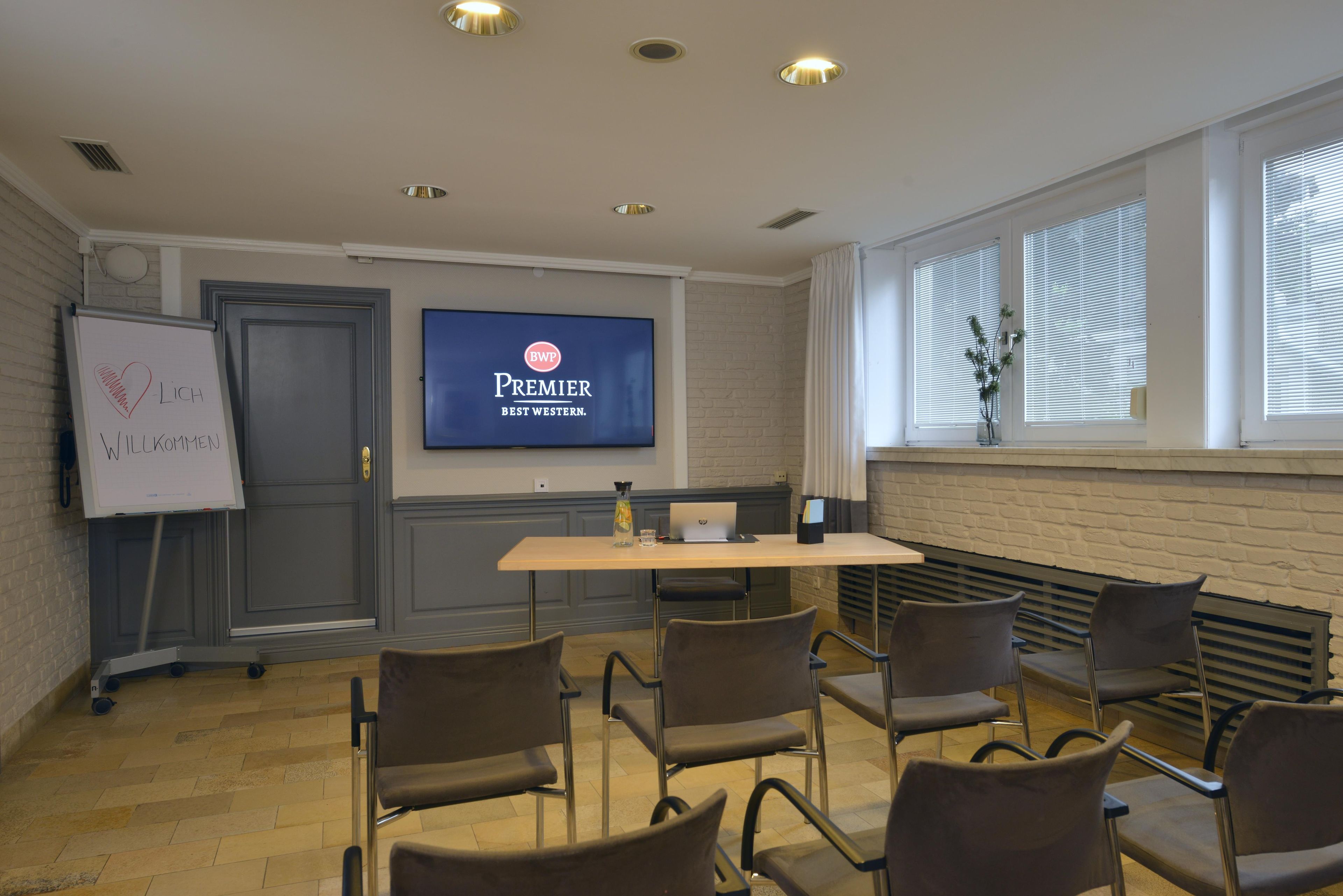 A conference room with a television displaying 'Premier Best Western' logo, a whiteboard with a heart and text, and a brick wall.