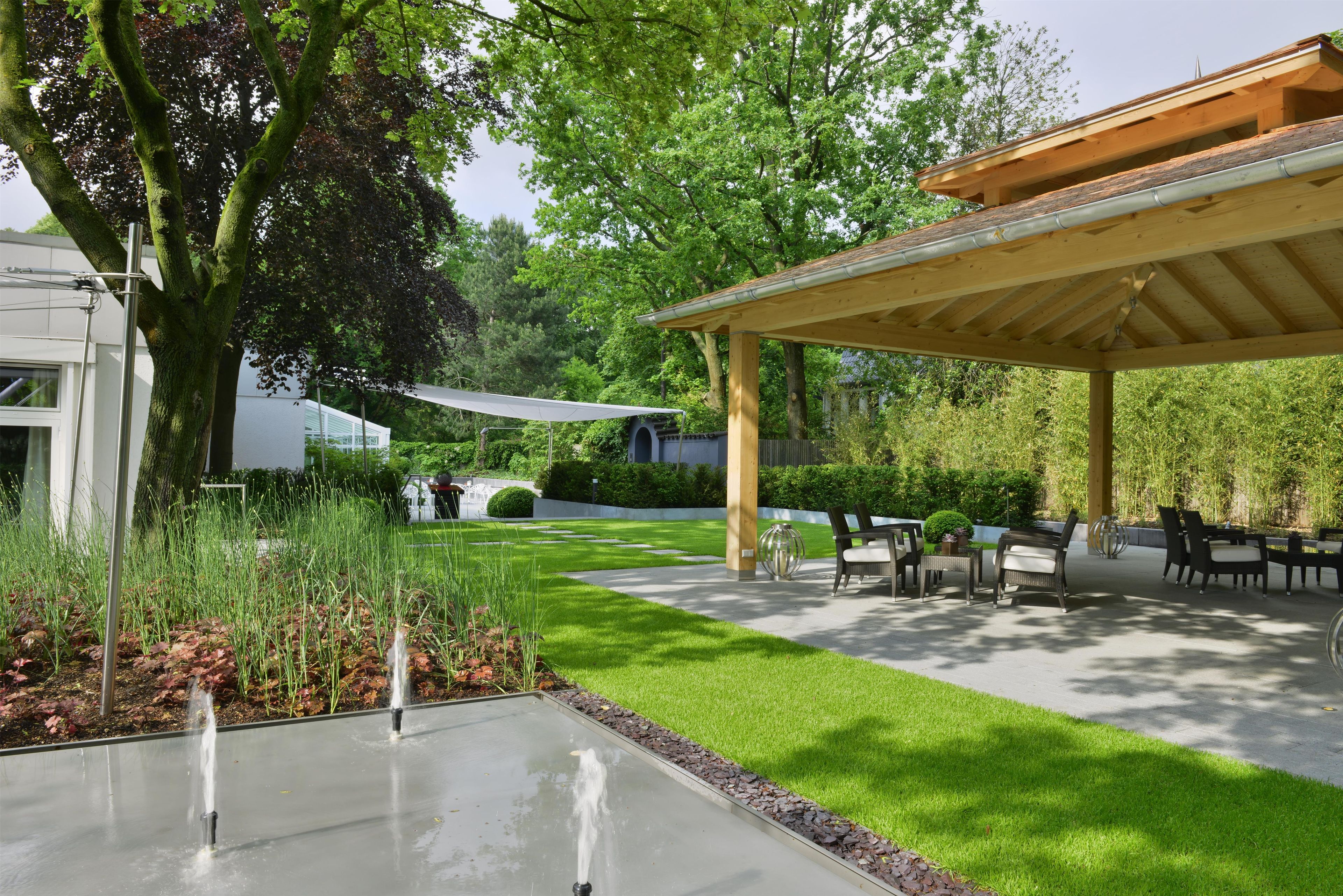 Un espacio de estar al aire libre cubierto con una pérgola, una fuente de agua y un césped bien cuidado.