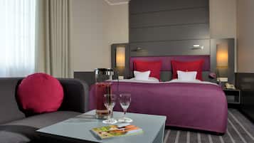 A hotel room with a bed, a nightstand, a coffee maker, a table with a magazine, and a sofa.