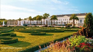 A formal garden with manicured lawns, geometric hedges, and classical statues.