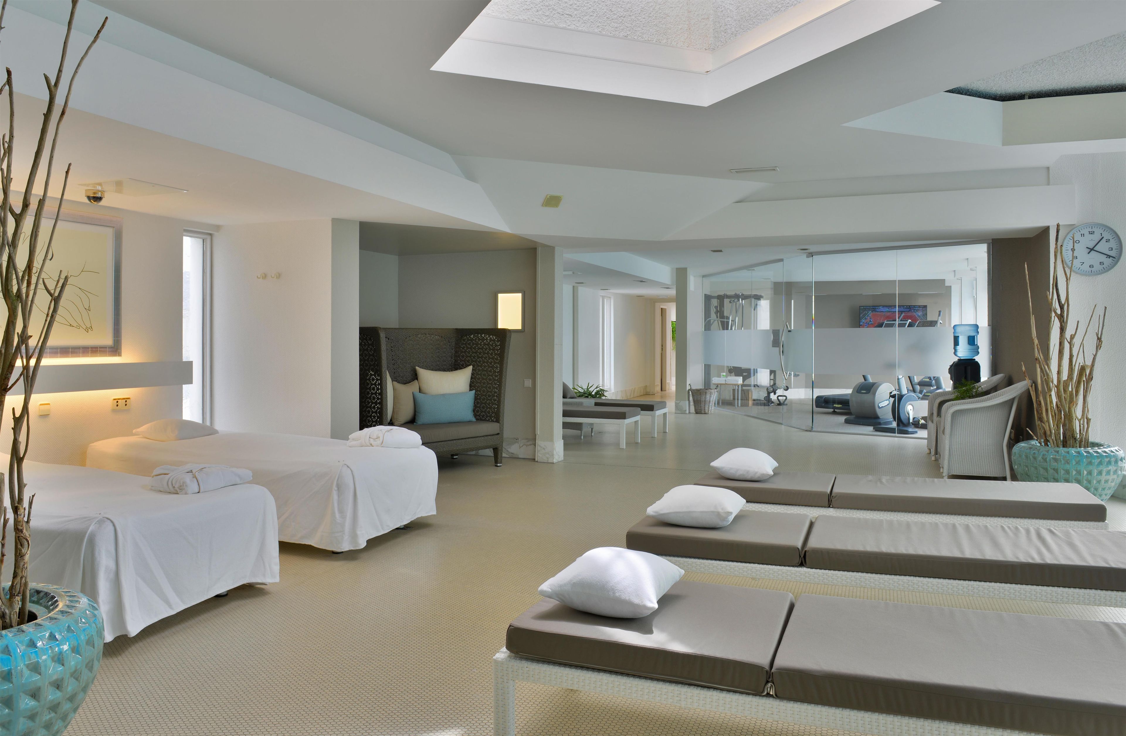 Ein Hotelzimmer mit zwei Betten, einer Sitzecke mit einer Couch und Sesseln, einem Fitnessbereich mit Trainingsgeräten und einem großen Fenster.