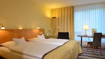 Ein Hotelzimmer mit Doppelbett, Nachttischlampen, einem Schreibtisch mit Stuhl und einem großen Fenster mit Vorhängen.