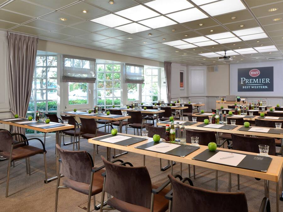 Un salón de conferencias con varias mesas, sillas y una pantalla de proyector mostrando 'Premier Best Western'.